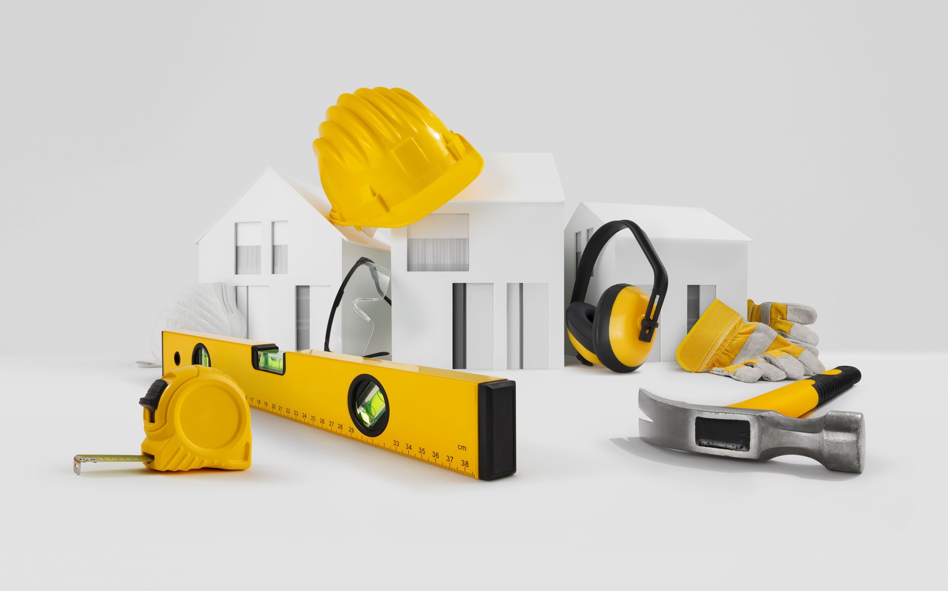 Concept de construction de maison. Outils pour les travaux de construction. Maisons modèles architecturaux, casque jaune, mètre et niveau à bulle au-dessus de la table avec écouteurs de sécurité, lunettes et gants. Réparation d’entretien à domici